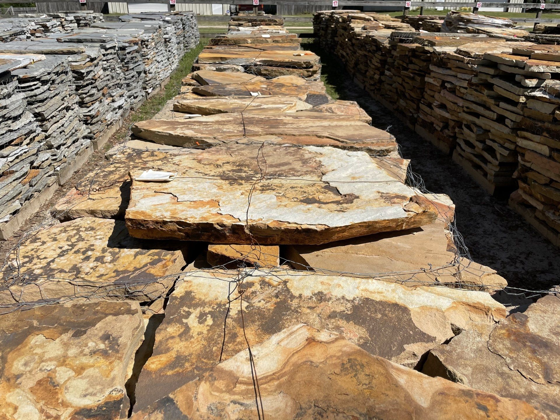 Stacks of tan, gray, and brown flagstone paving stones in an outdoor yard.
