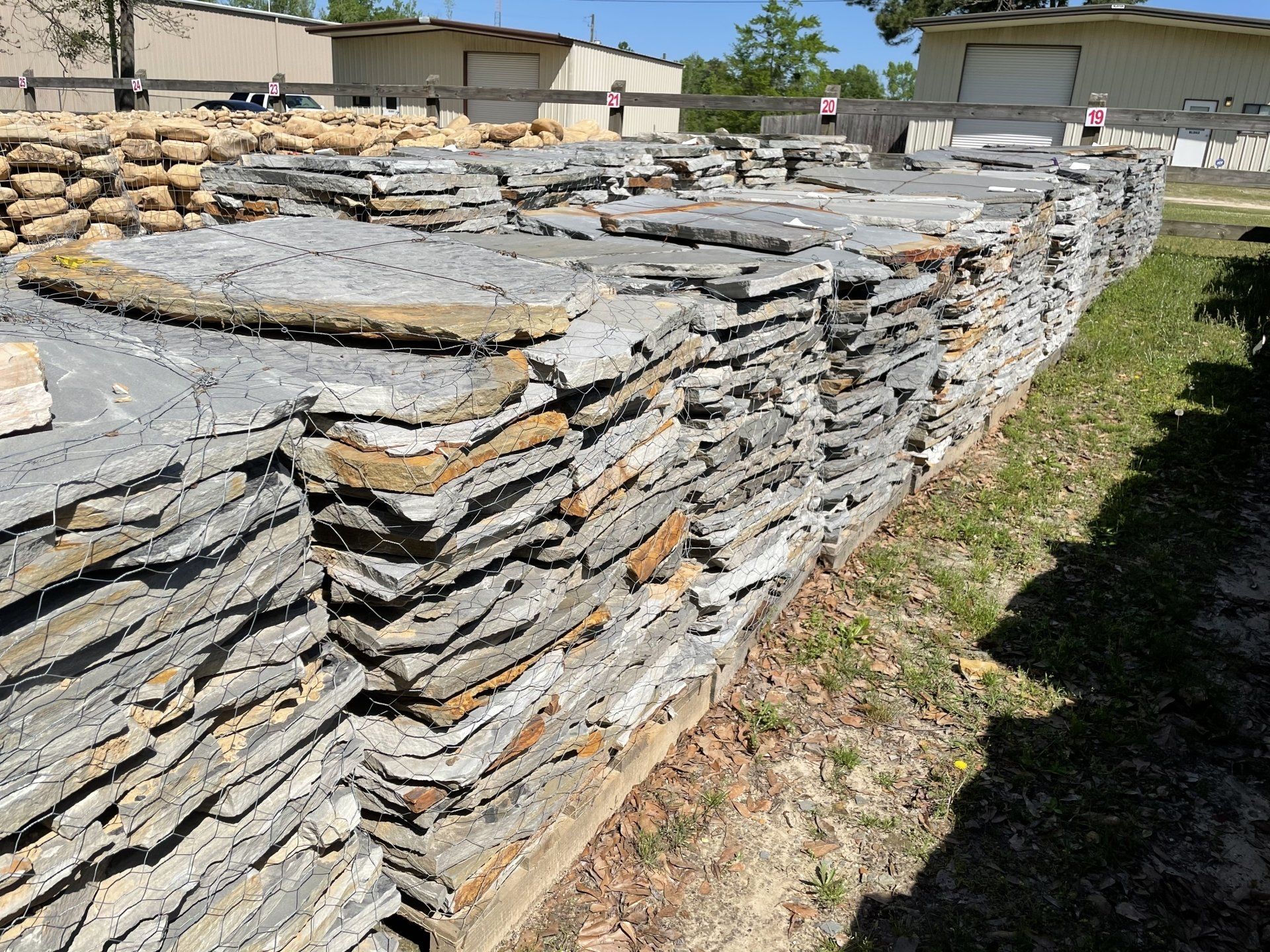 Stacks of gray and tan flagstone pavers outside a building, ready for use.