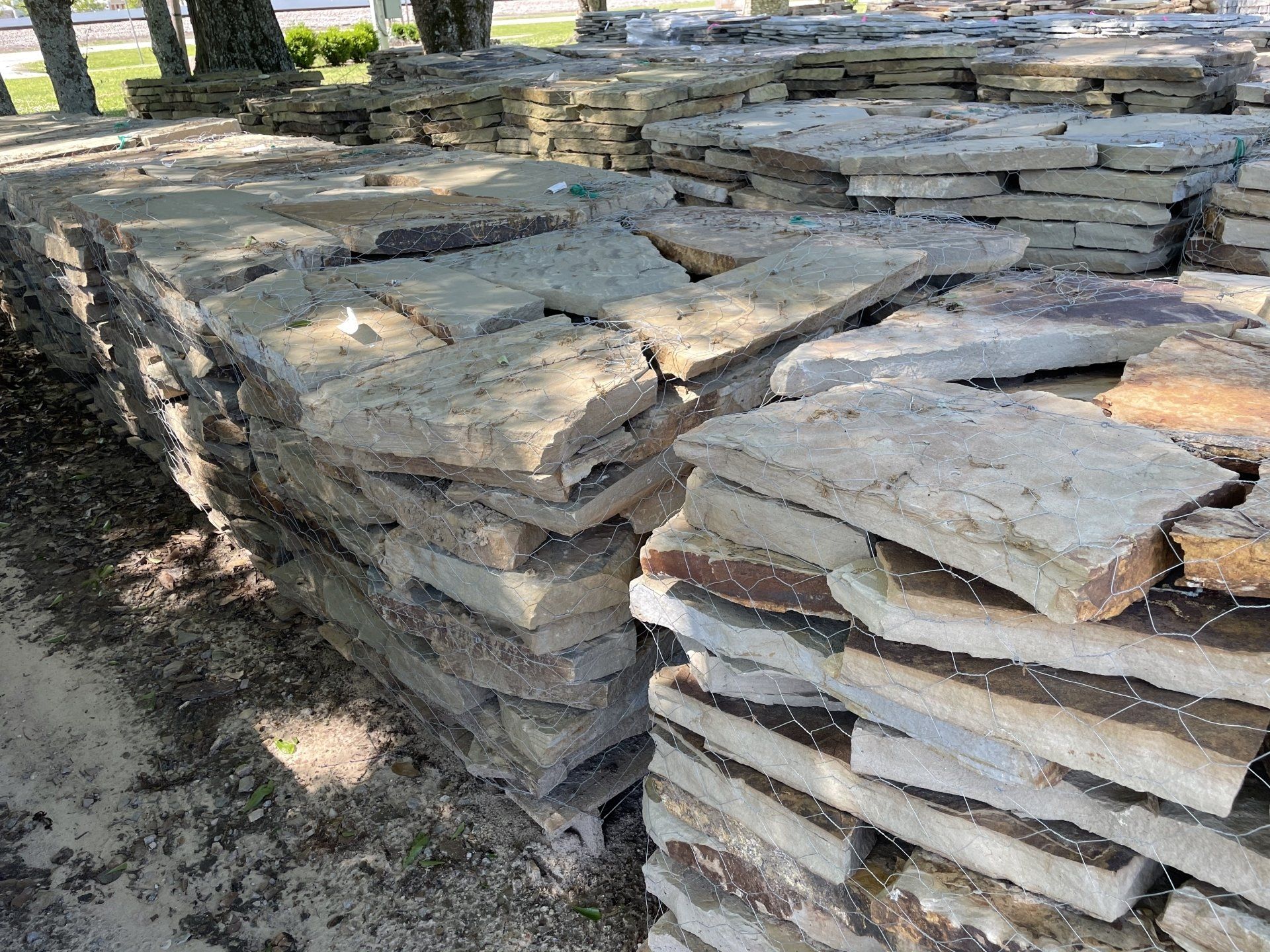 Stacks of rectangular, light brown and gray flagstones on pallets, outdoors.