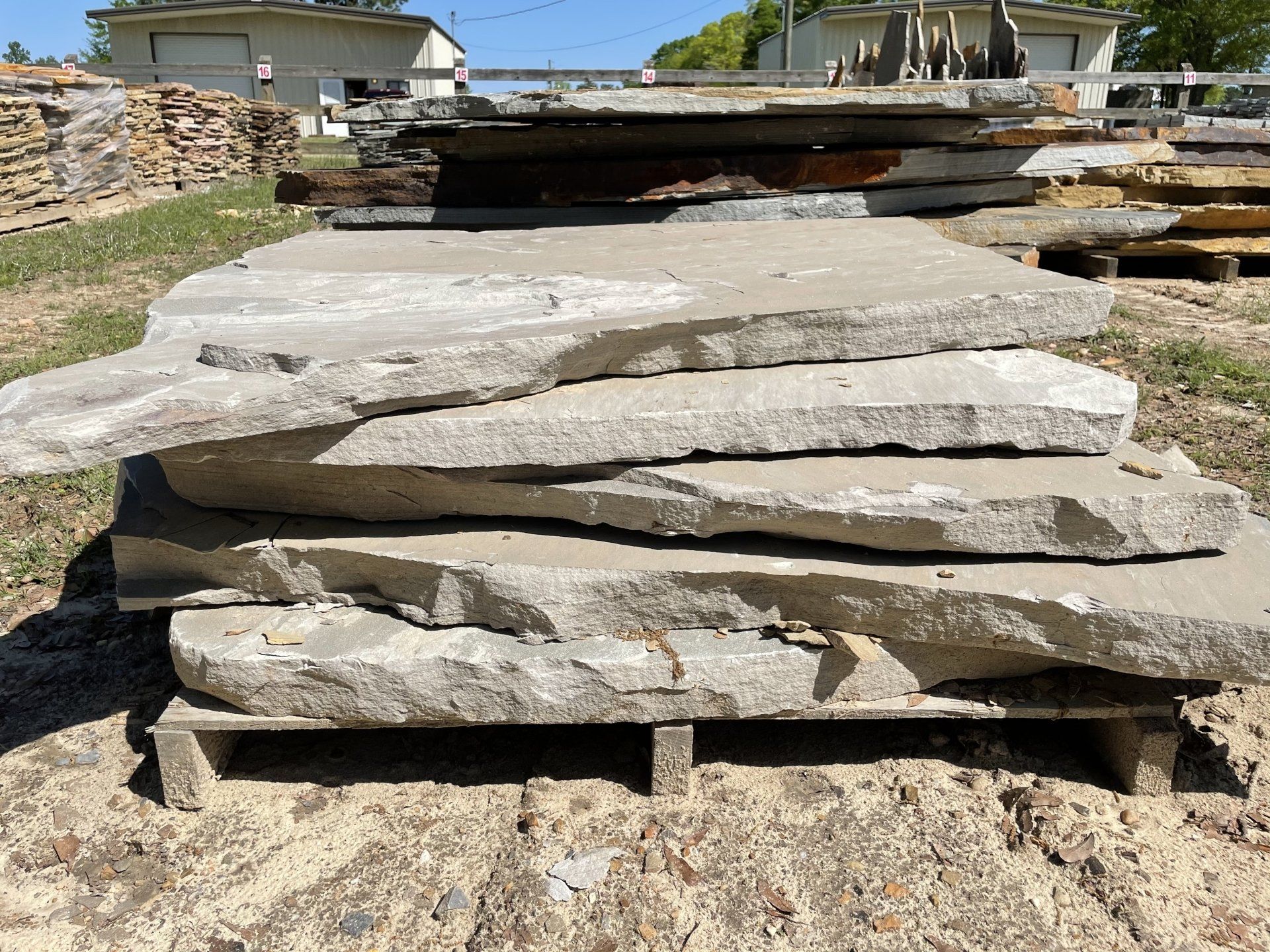Gray stone slabs stacked on a wooden pallet, outdoors in a yard.