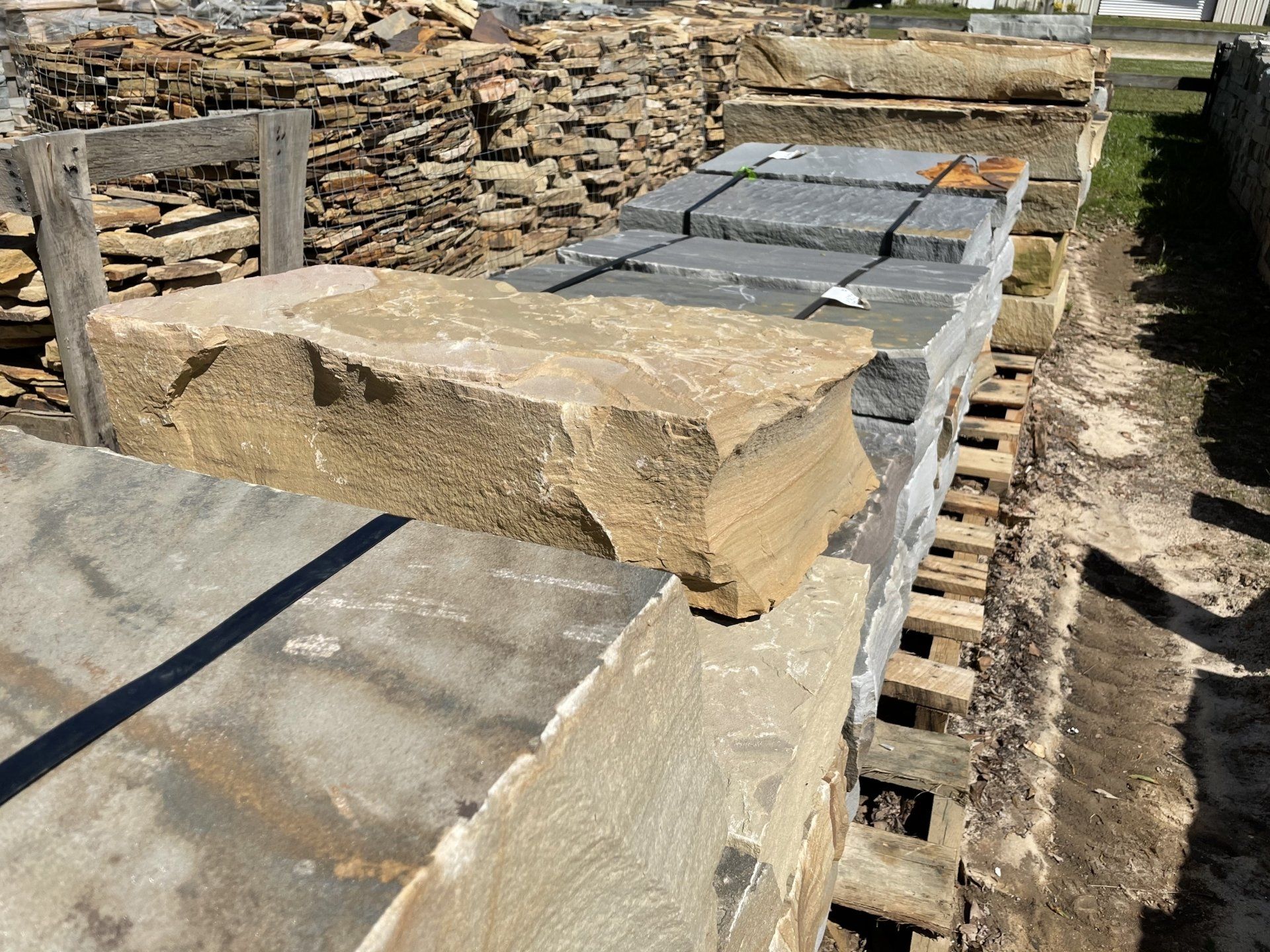 Stone blocks for construction, stacked outdoors. A tan slab rests on gray and black stone.