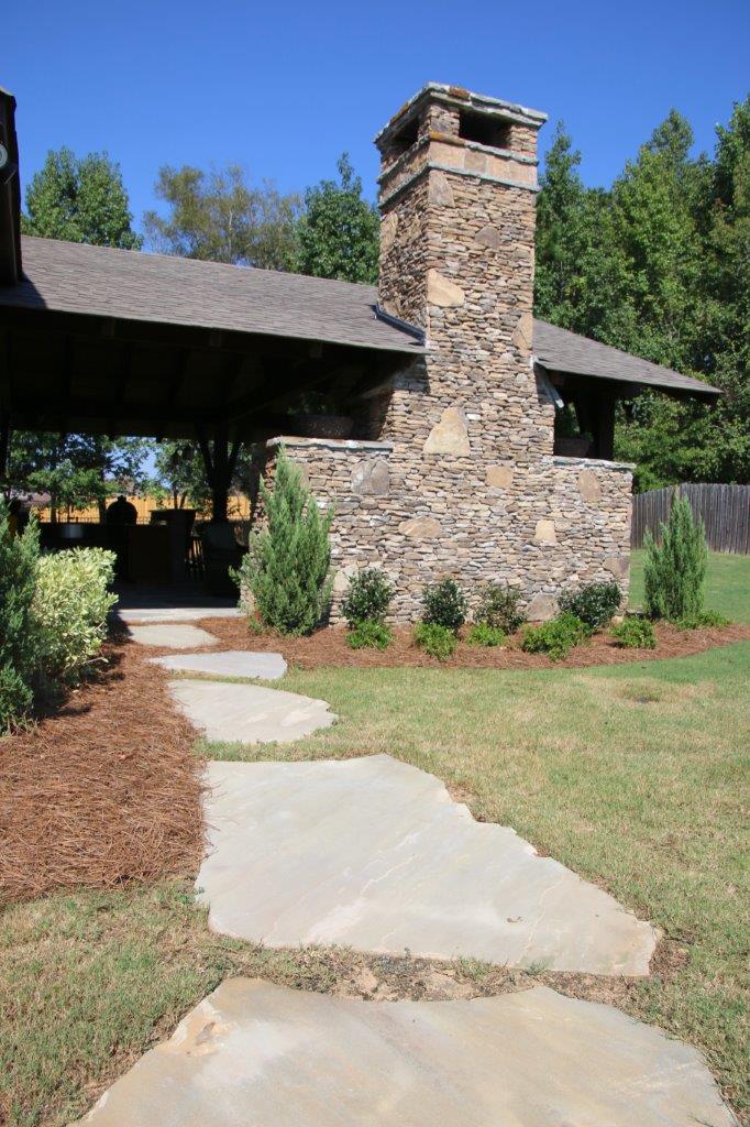 Stone path leads to a covered outdoor structure with a stone chimney and landscaping.