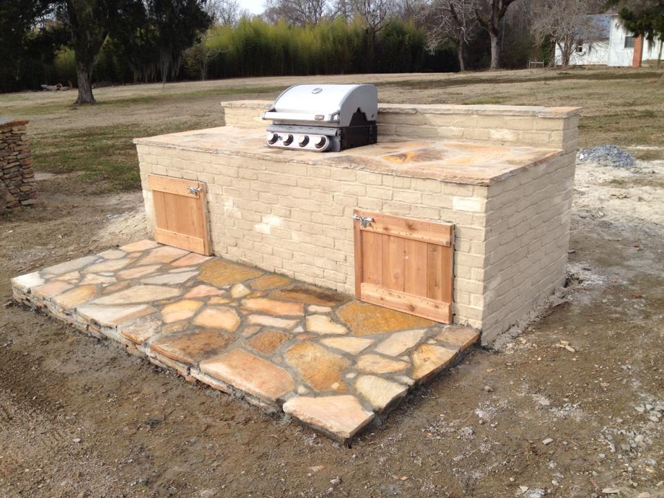 A grill is sitting on top of a brick counter in a yard.