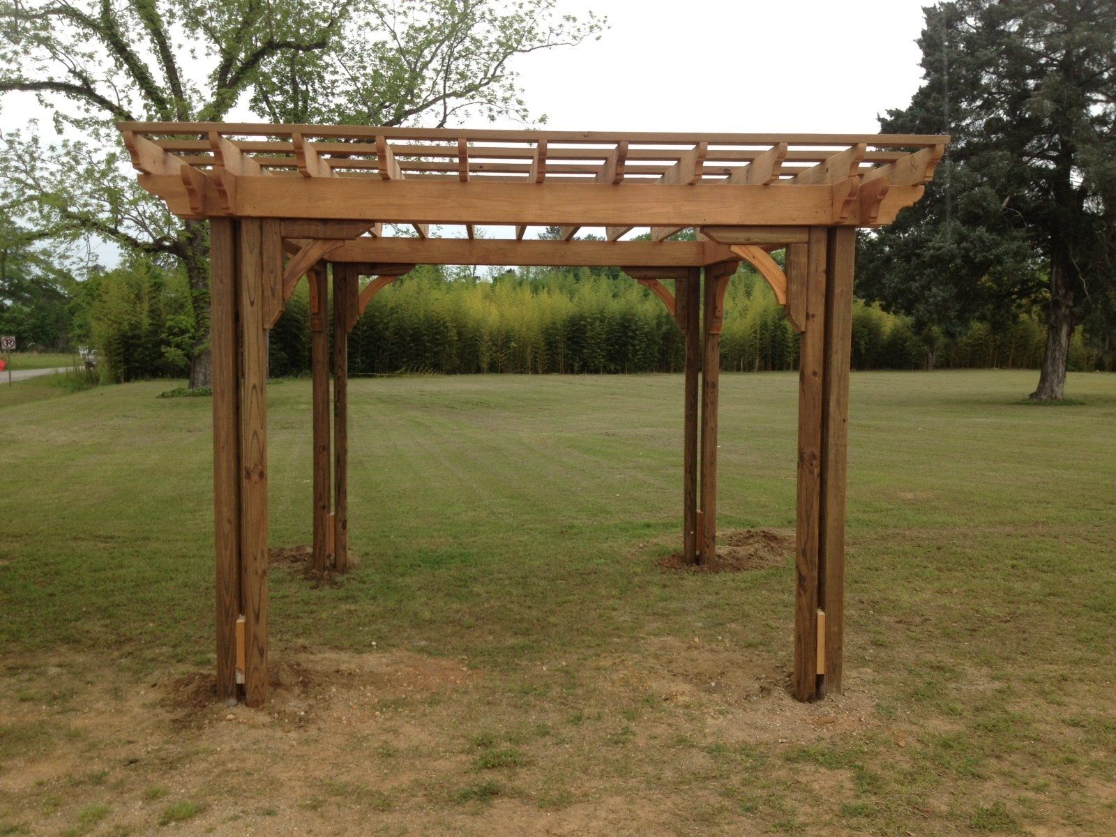Wooden pergola in a grassy yard with trees in the background.