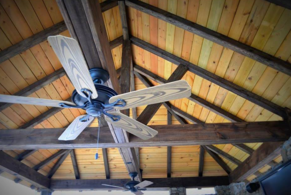 Wooden vaulted ceiling with a ceiling fan in an outdoor setting.