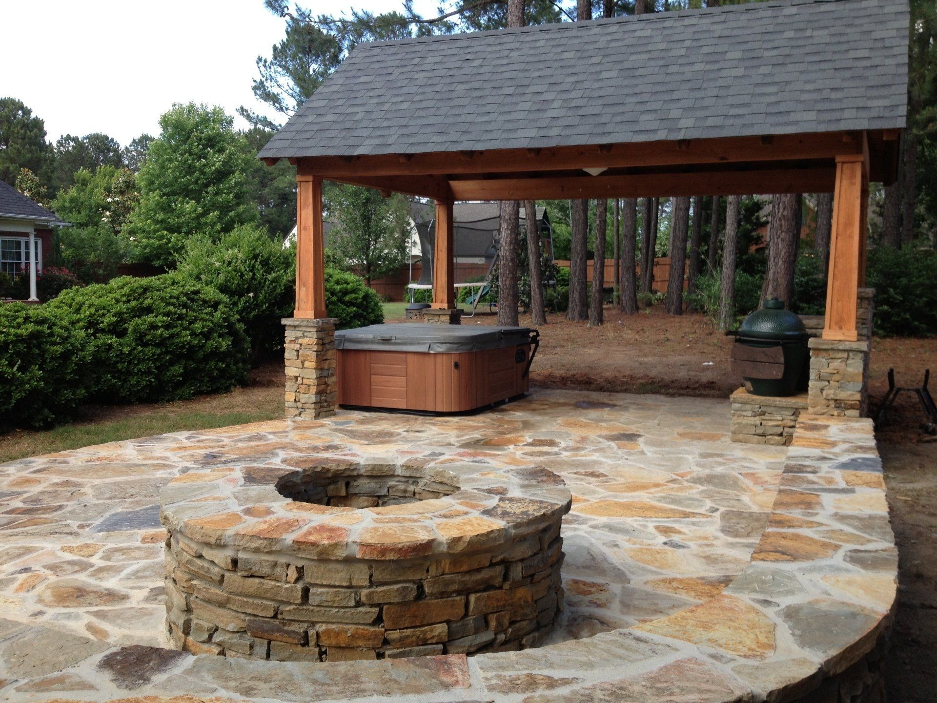 Stone patio with fire pit and hot tub under a wooden gazebo.