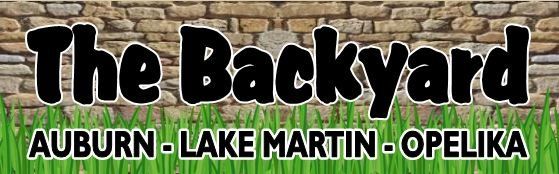 The Backyard logo. Black bubble letters over a brick wall with grass and the words 