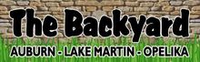 The Backyard logo. Black bubble letters over a brick wall with grass and the words 