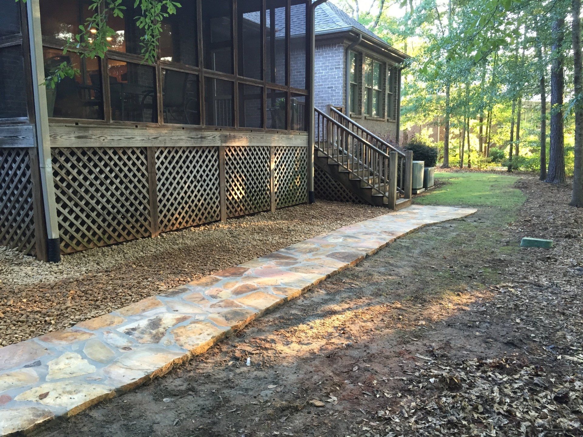 Stone pathway leads to a house with a screened porch in a wooded area.