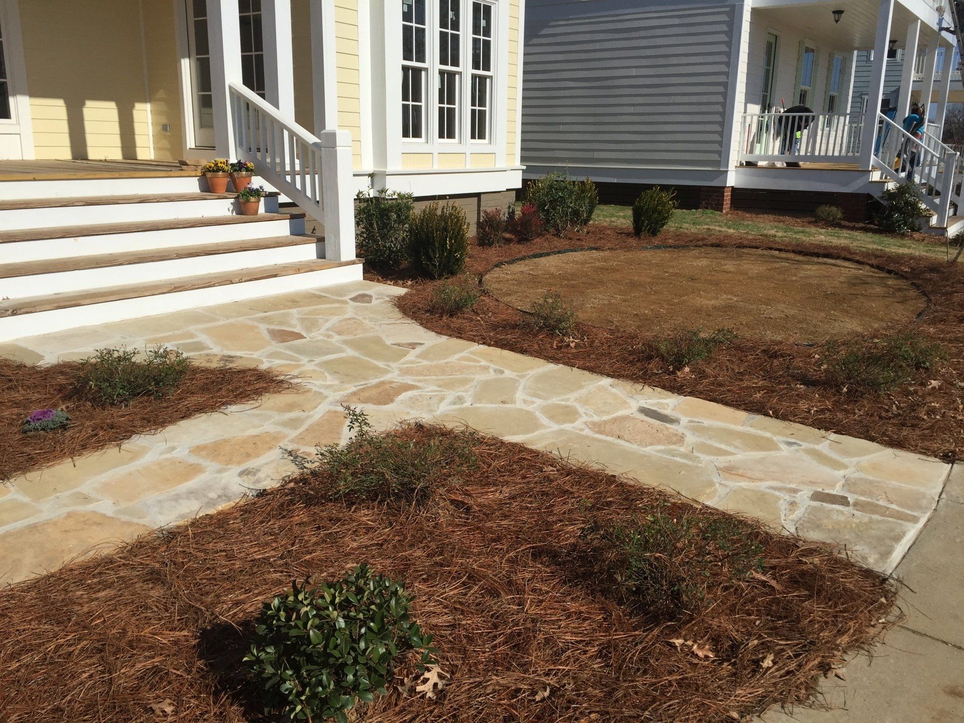 Flagstone pathway leading to a yellow house's porch, surrounded by mulch and shrubs.