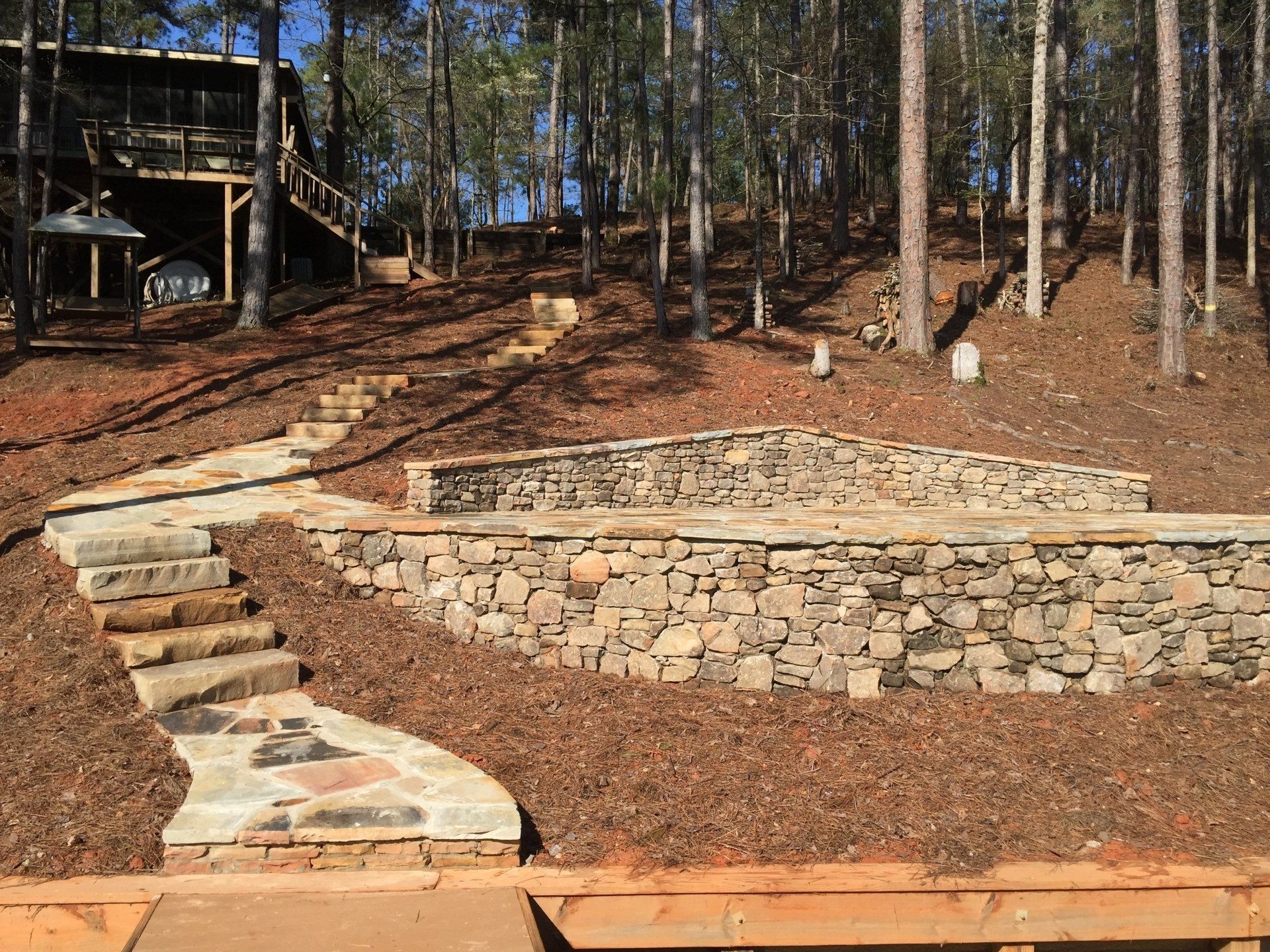 Stone steps and paths lead to a stone stage on a hillside in a forest.