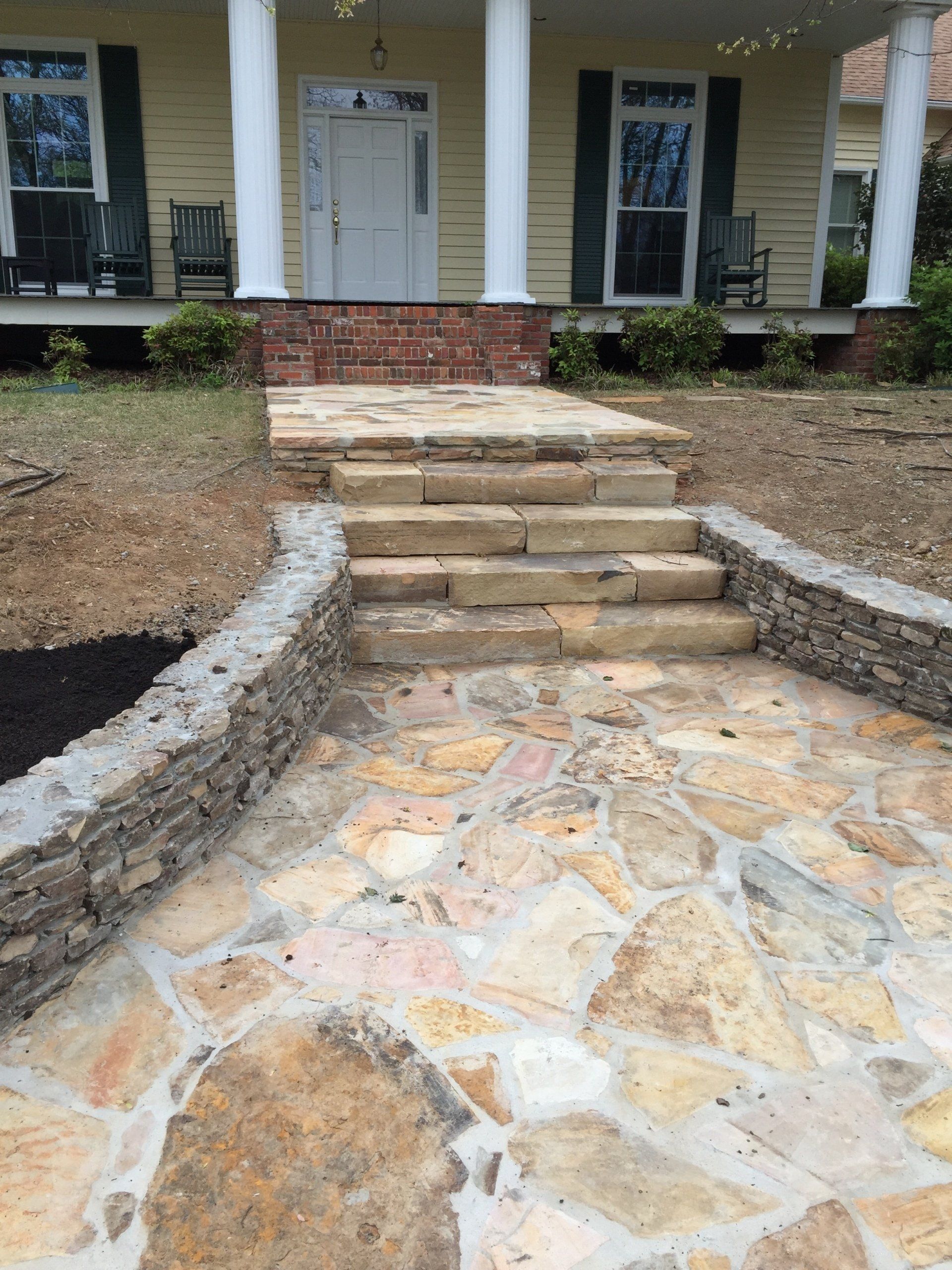 Stone pathway and steps leading to a yellow house with white columns.