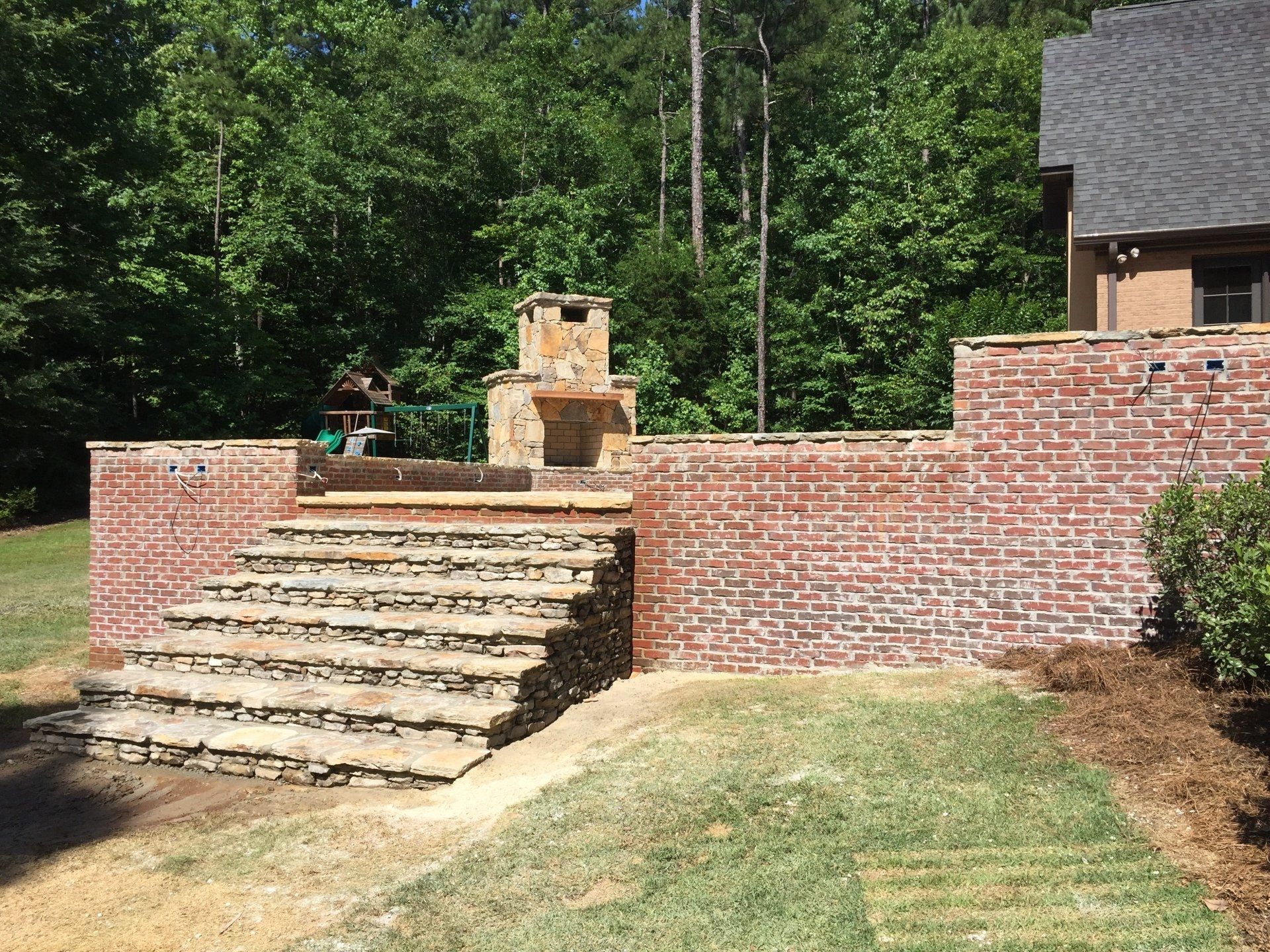 Brick patio with stone steps leading to a brick wall and fireplace; backyard setting.