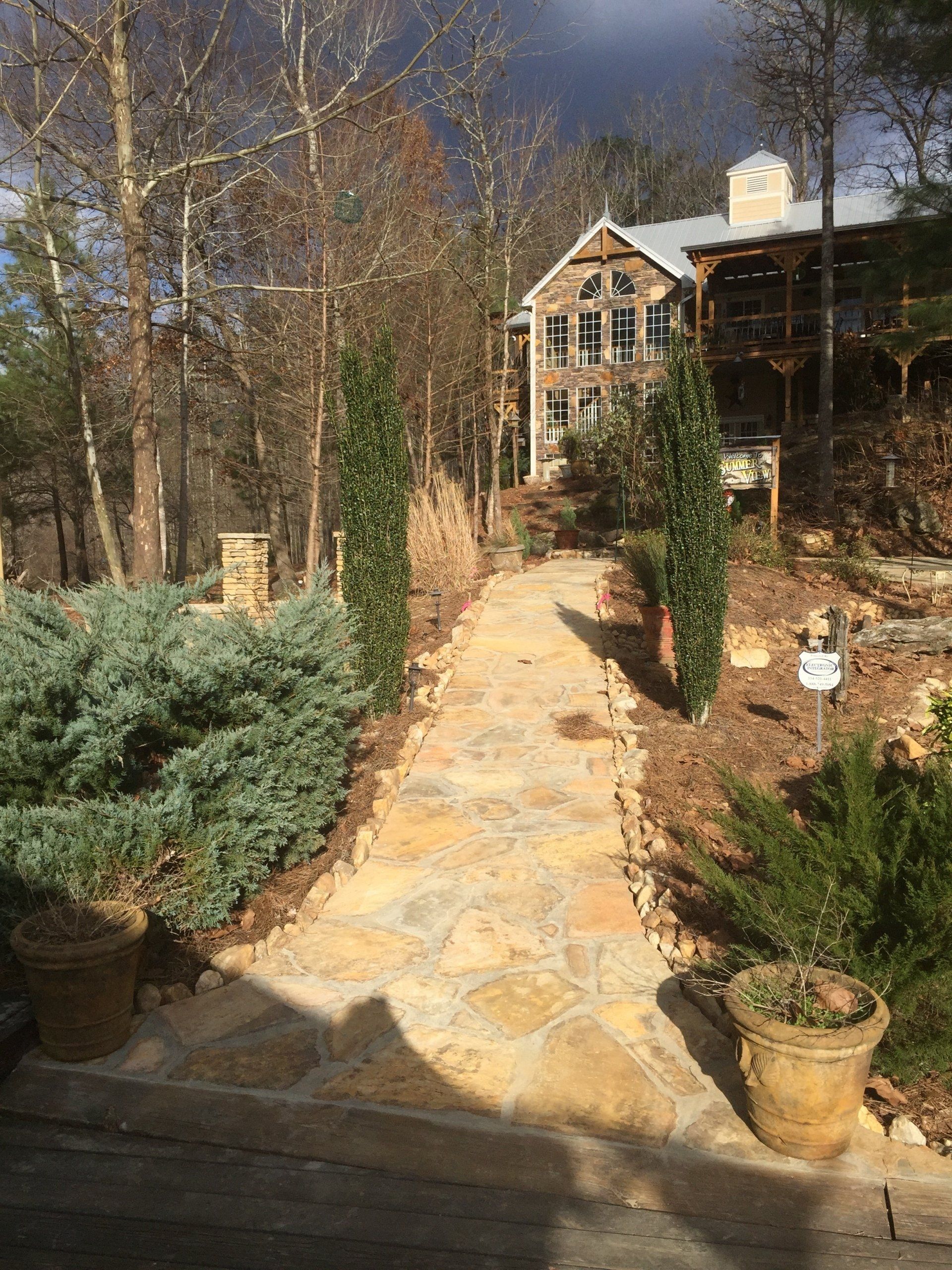 Stone path leading up to a multi-story cabin in a wooded setting, with plants and trees along the path.