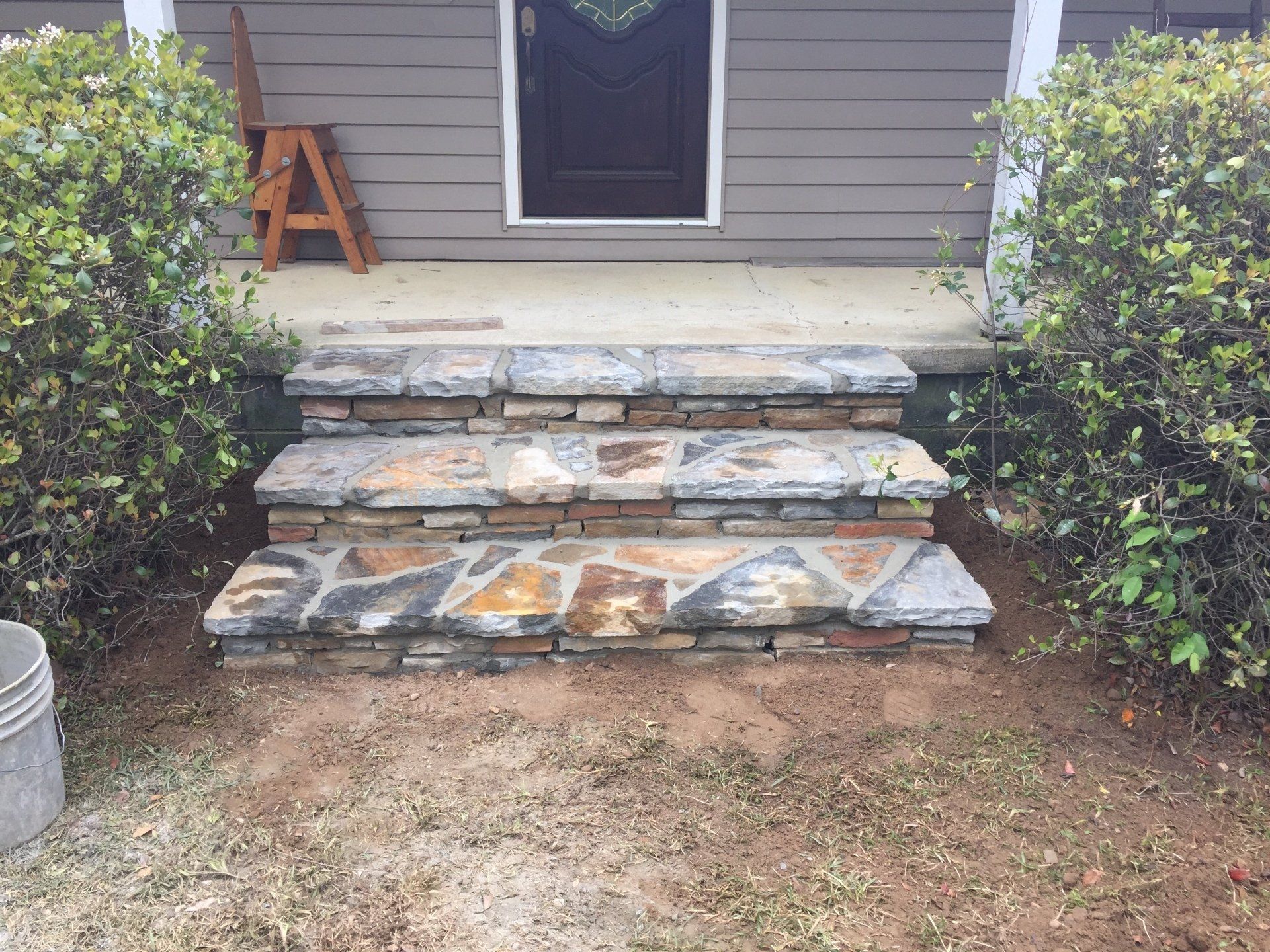 Stone steps leading to a front door, flanked by bushes, in front of a house.