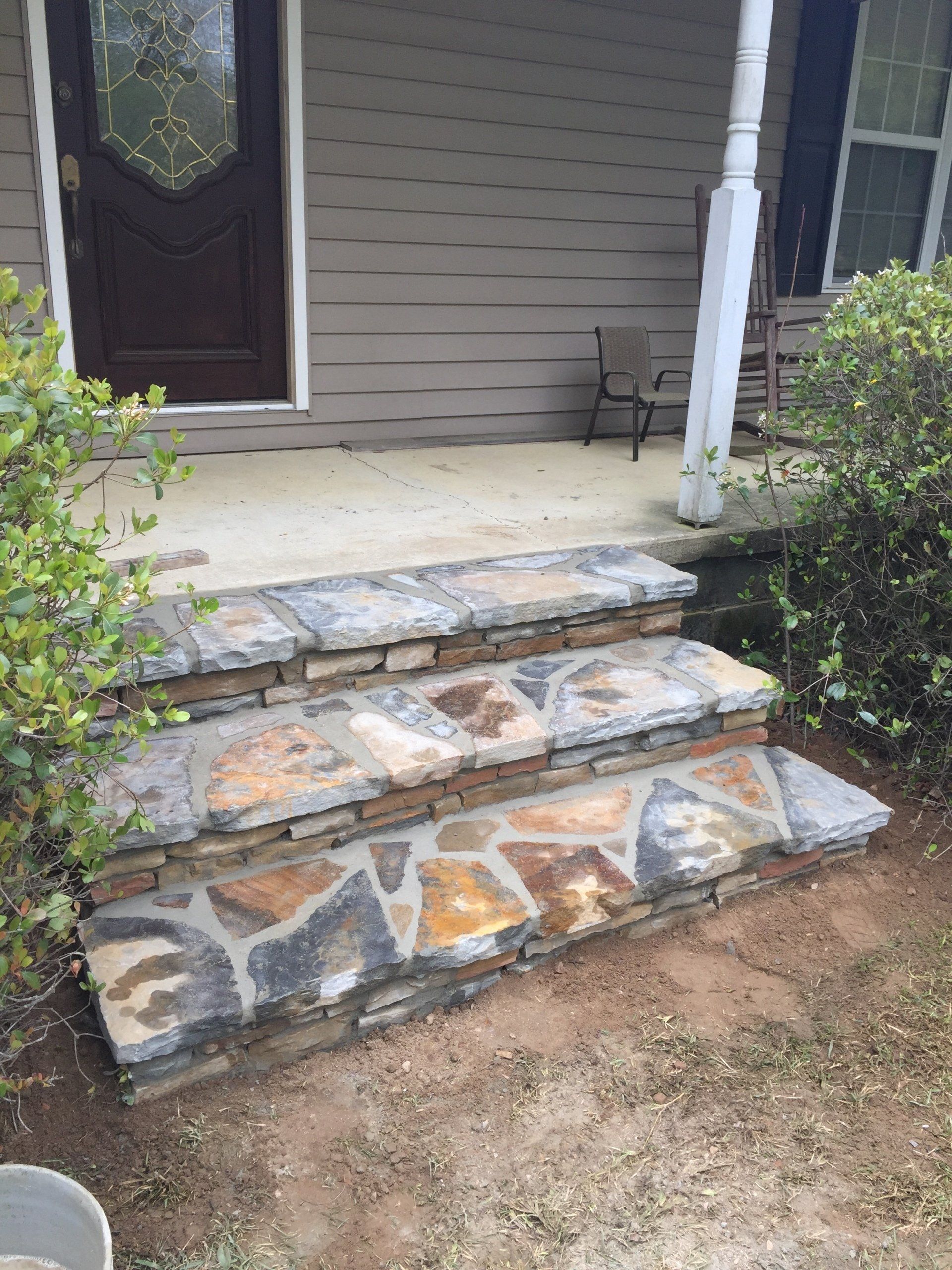 Stone steps leading up to a house's porch with a brown door.