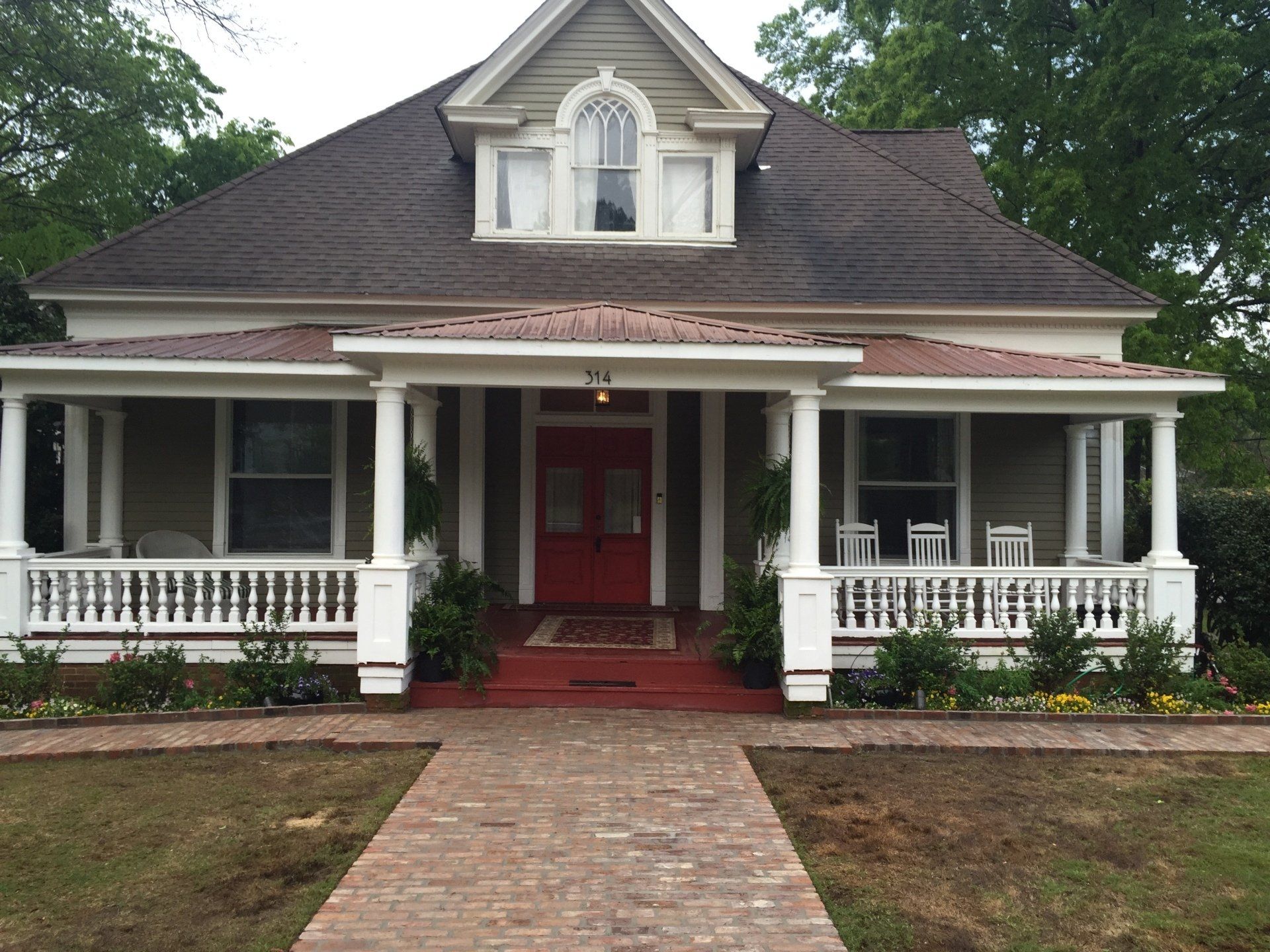 Victorian house with a red front door, a covered porch, and a brick walkway.