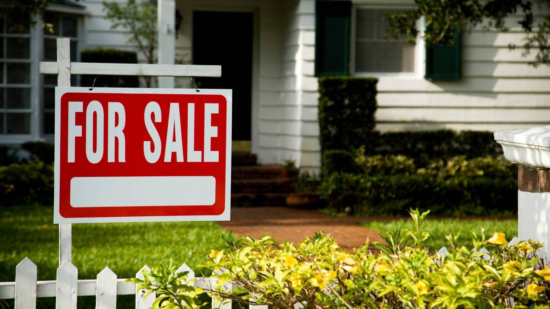 A for sale sign is hanging in front of a house.