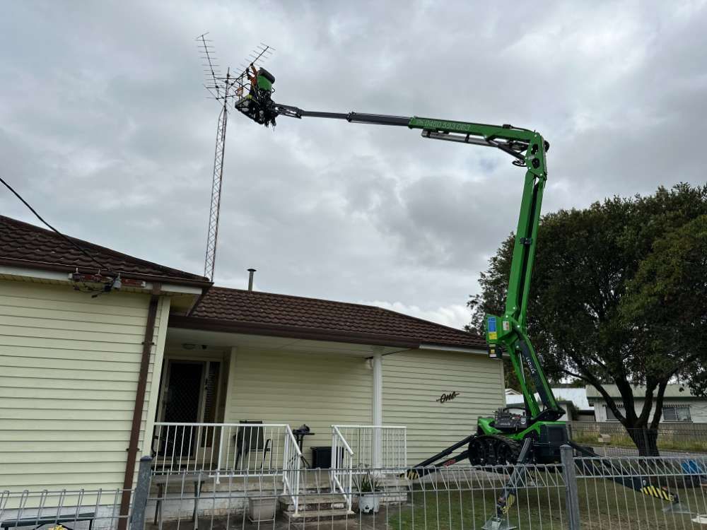 A Green Crane Is Working On An Antenna In Front Of A House — High Work Services in Maitland, NSW