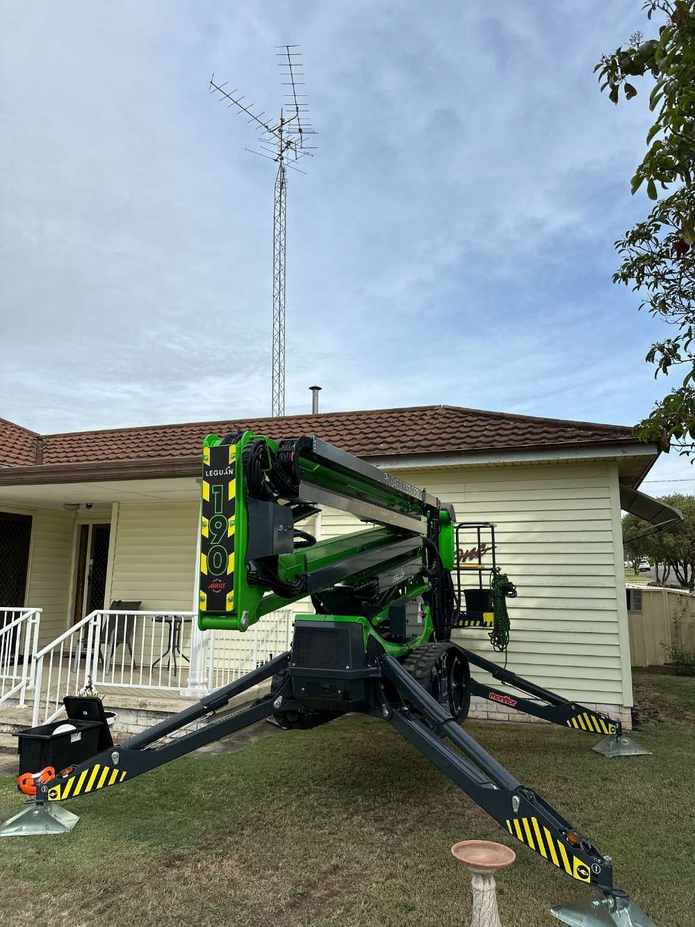 A Green Crane Is Sitting In Front Of A House — High Work Services in Maitland, NSW