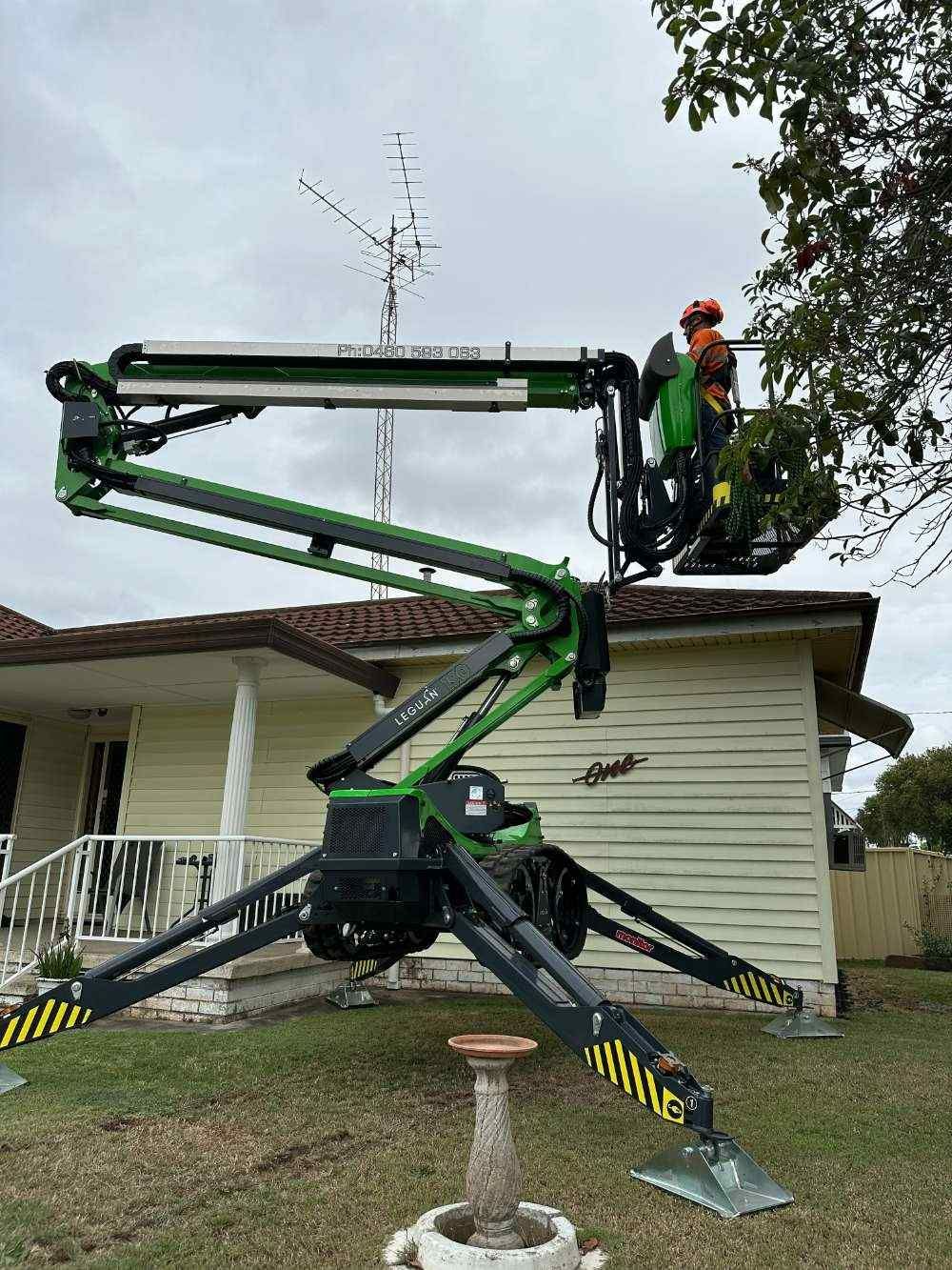 A Green Crane Is Working On An Antenna In Front Of A House — High Work Services in Maitland, NSW