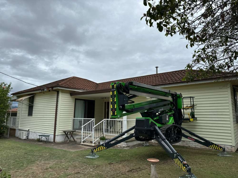 A Green Crane Is Parked In Front Of A House — High Work Services in Maitland, NSW