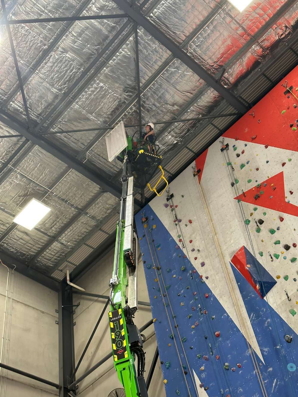 A Man Is Working On A Climbing Wall In A Gym — High Work Services in Maitland, NSW