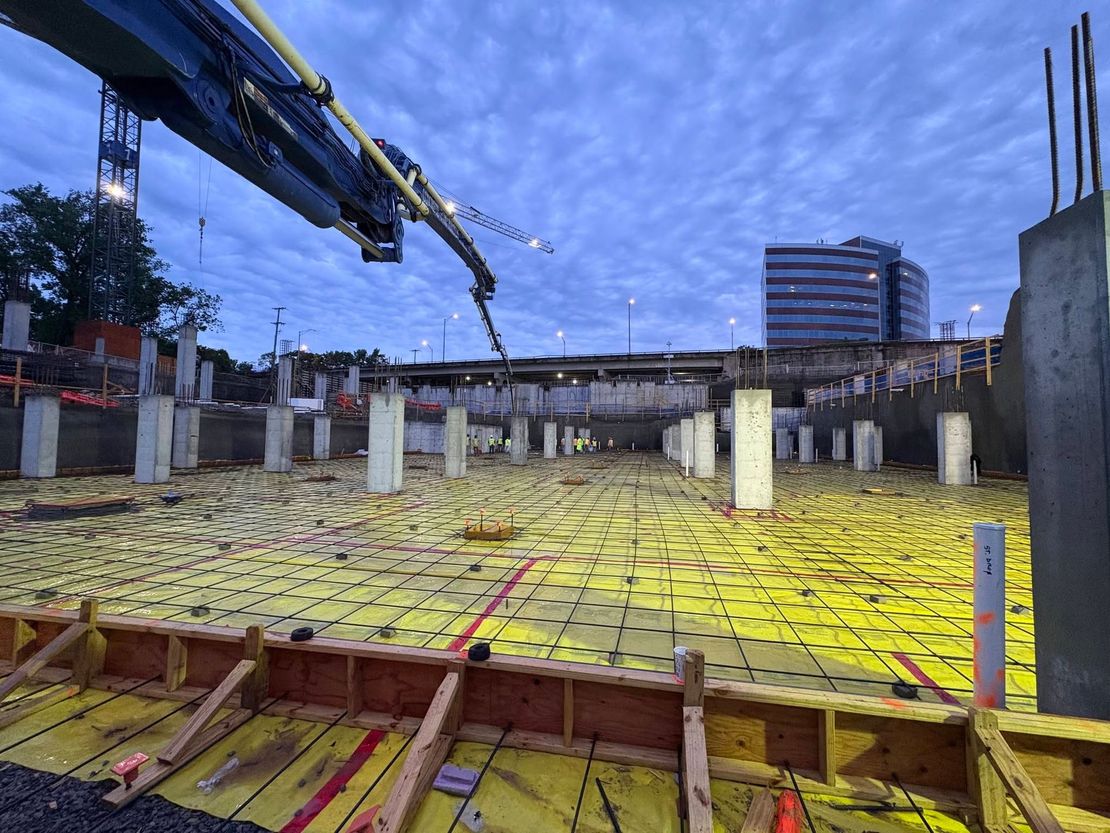 Construction site with concrete foundation, yellow waterproofing, and crane at dusk