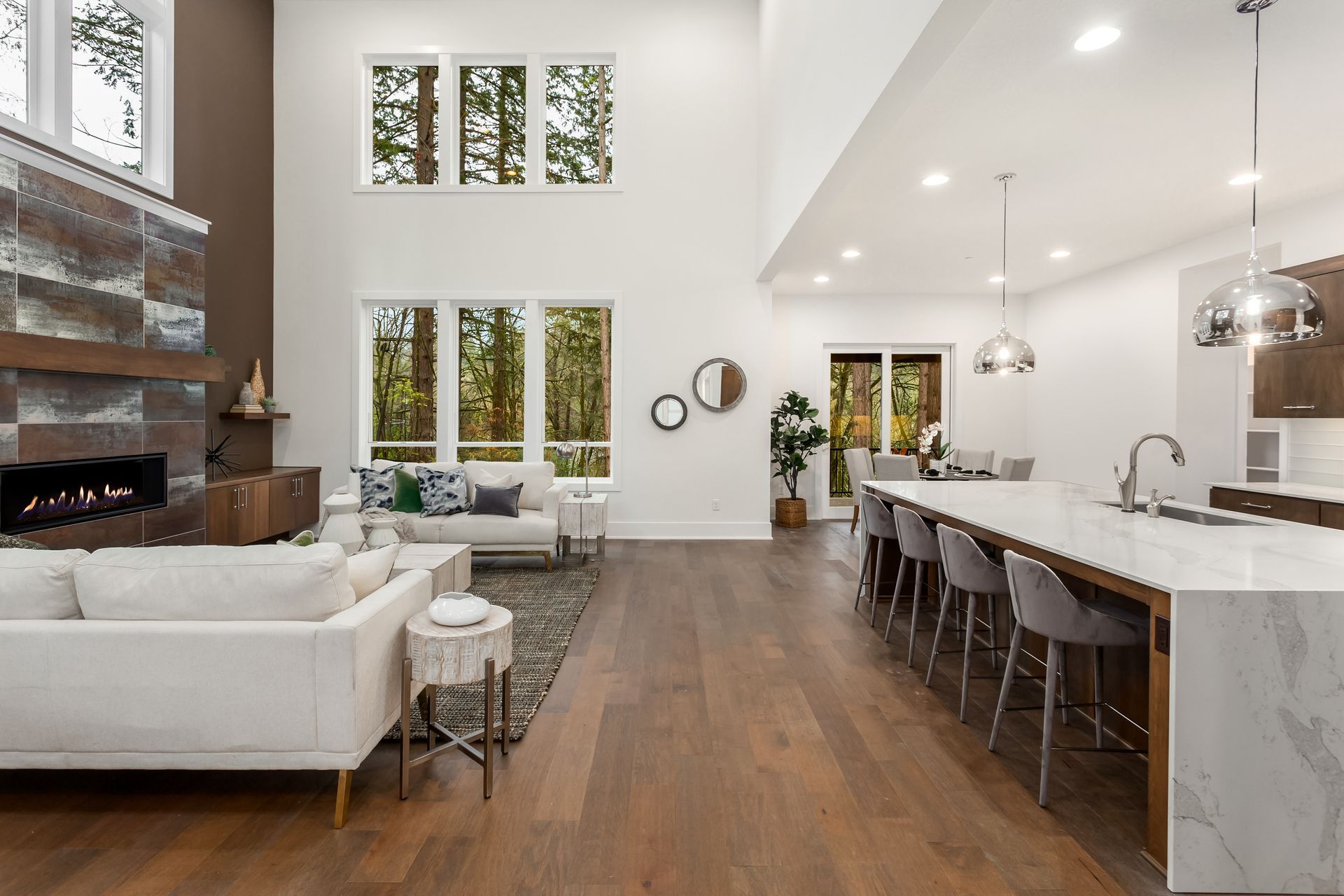 Bright open-concept living room and kitchen with white furniture, wood floors, and tall windows
