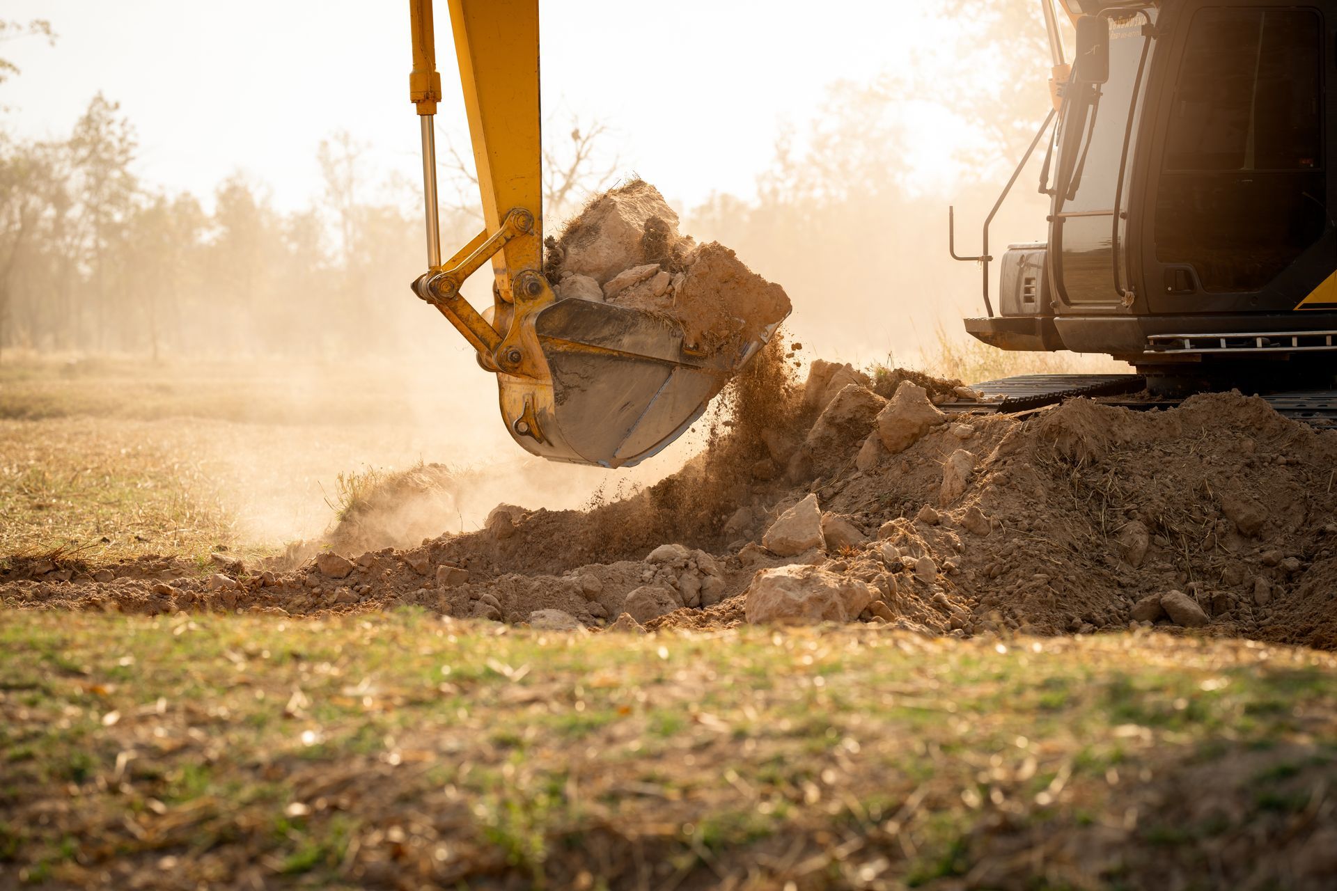Excavator bucket scooping dirt at a construction site in warm sunlight