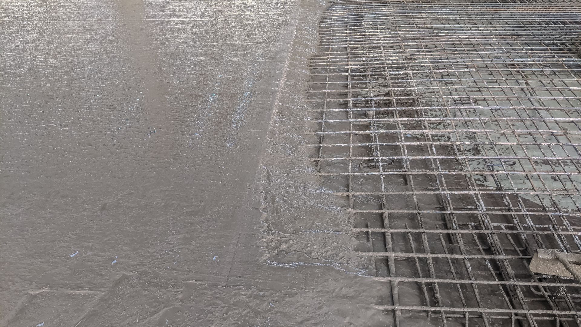 Wet concrete being poured beside a metal wire grid reinforcement.