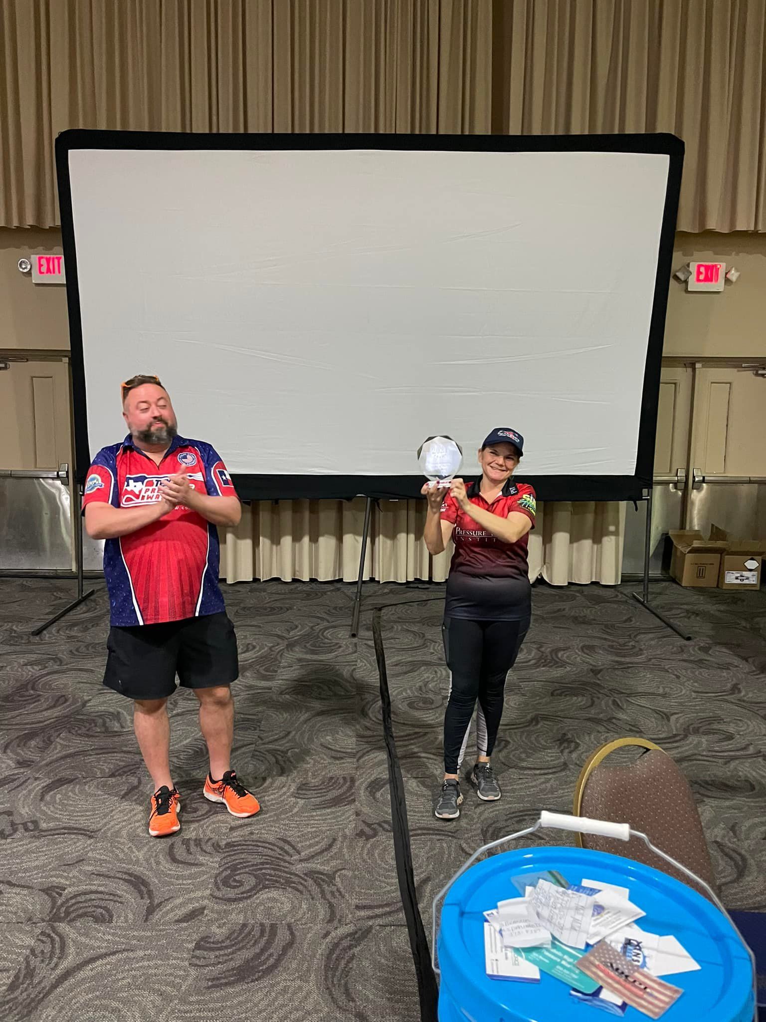 A man and a woman are standing in front of a large screen in a room.
