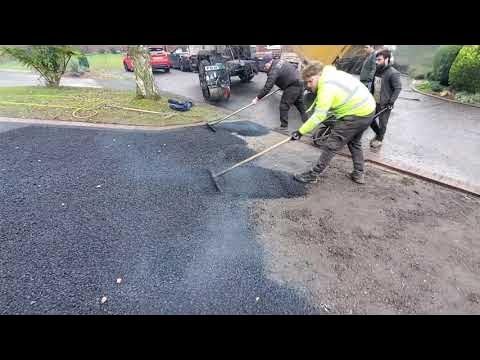 Road crew laying asphalt on a driveway. Workers use rakes to smooth black material.