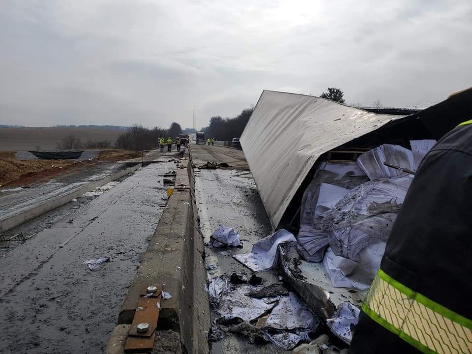A man is standing next to a truck that has fallen off the road.