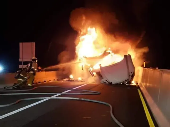 A truck is on fire in the middle of the road.