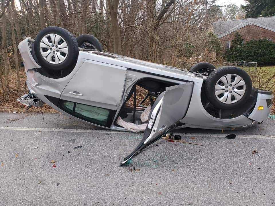 A silver car is upside down on the side of the road.