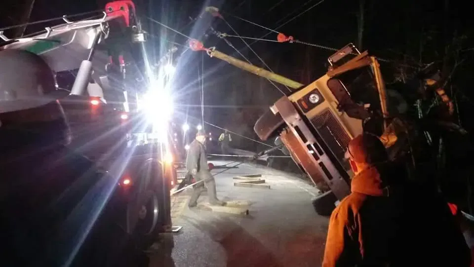 A truck is being towed by a crane at night.