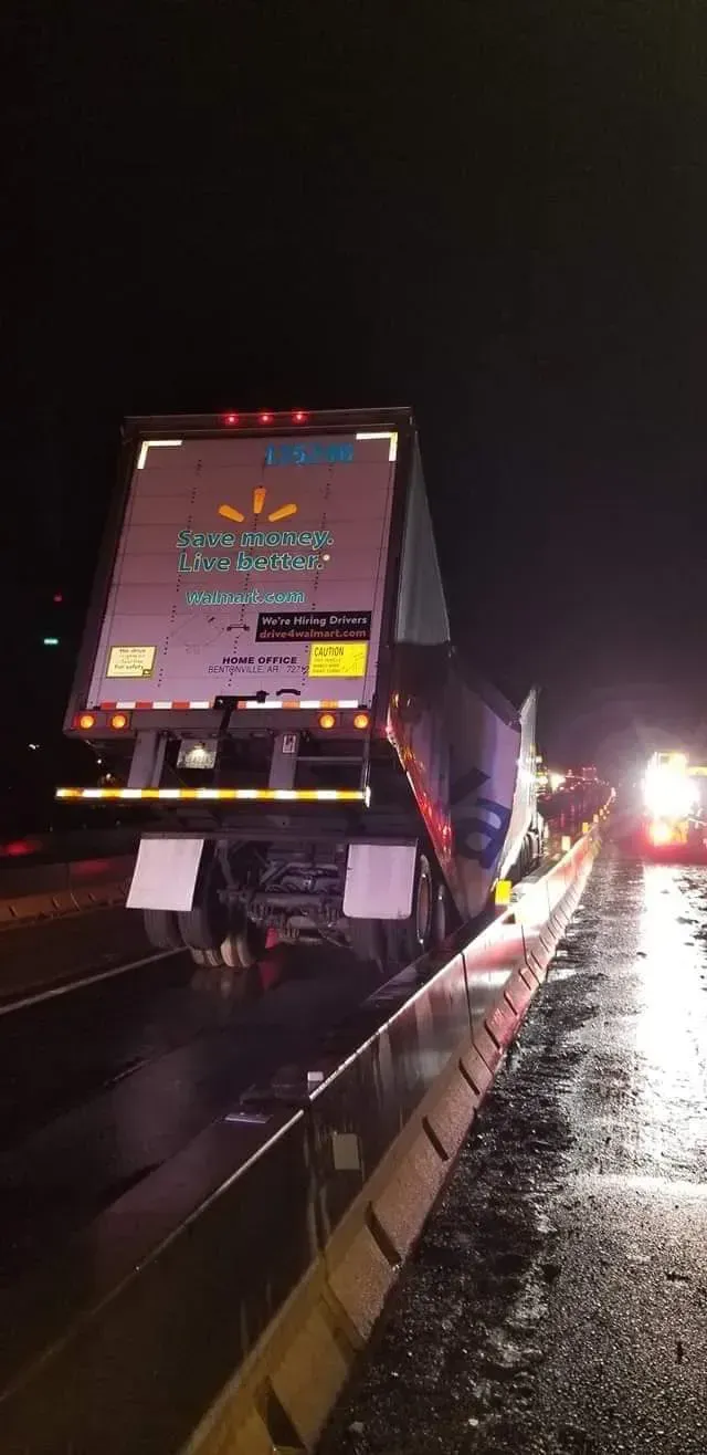 A semi truck is sitting on the side of a highway at night.