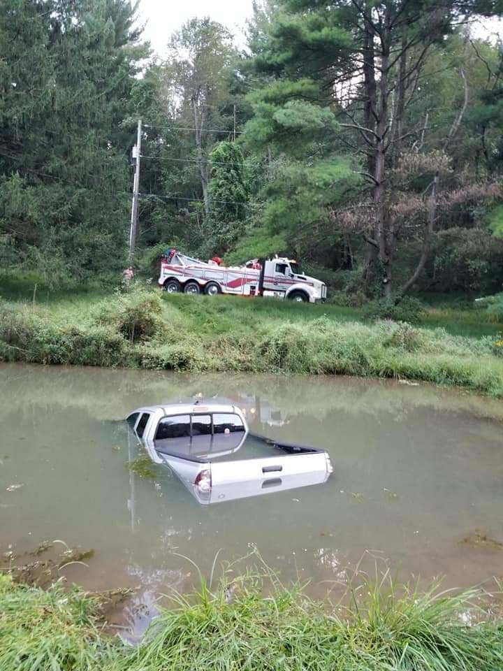 A truck is stuck in a pond with a tow truck in the background.