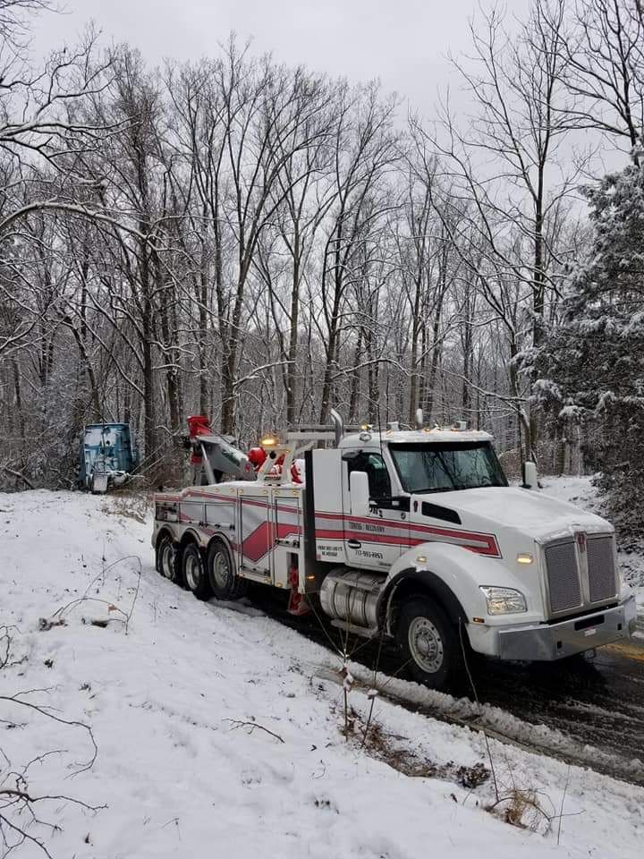 A white tow truck is driving down a snowy road.