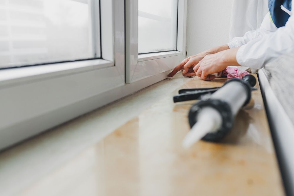 A Person is Applying Sealant to a Window Sill — Southside Glass & Aluminium In Bentley Park, QLD