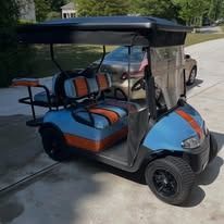 Blue and orange golf cart parked on a sunny street, with black roof and seats.