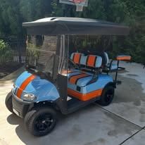 Orange and blue golf cart parked on a driveway outdoors with trees in the background