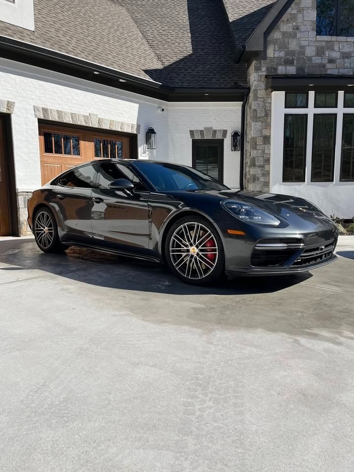 Black sports coupe parked in a driveway beside a white house and garage