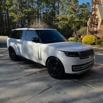 White SUV parked on a driveway with trees and a house in the background