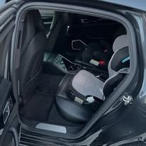Car interior with black child safety seats in the back seat, rear door open.