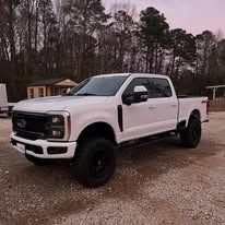 White lifted pickup truck parked on gravel in front of a house with trees in the background