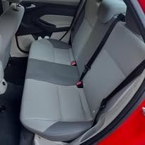 Gray rear car seat with black trim and red seatbelt buckles inside a red vehicle