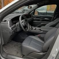 Open car interior with black leather seats and dashboard, viewed from the driver’s side door.