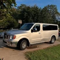 White passenger van parked on a driveway beside a grassy yard and trees in bright daylight